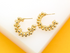 A pair of textured gold half-hoop earrings featuring clustered bead details rests on a white and yellow surface.