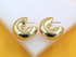 A pair of chunky gold hoop earrings rests neatly on a white display surface against a vibrant orange background.