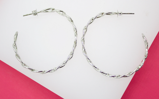 A pair of polished silver twist hoop earrings rests against a white and pink background.