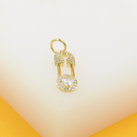 A gold safety pin pendant adorned with sparkling pave diamonds and a central crystal rests on a light background.
