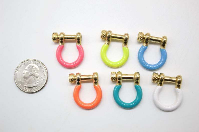 Six colorful enamel horseshoe shackles with gold-plated screw pins sit beside a US quarter for scale.