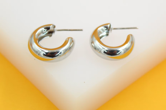A pair of shiny silver dome hoop earrings rests on a white display surface against a vibrant yellow backdrop.