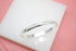 A polished silver baby bangle bracelet rests on a white block against a soft pink background.