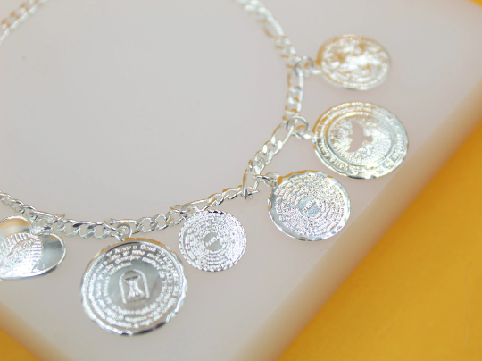 A sterling silver charm bracelet featuring intricate religious medallions and a heart pendant rests on a soft surface.