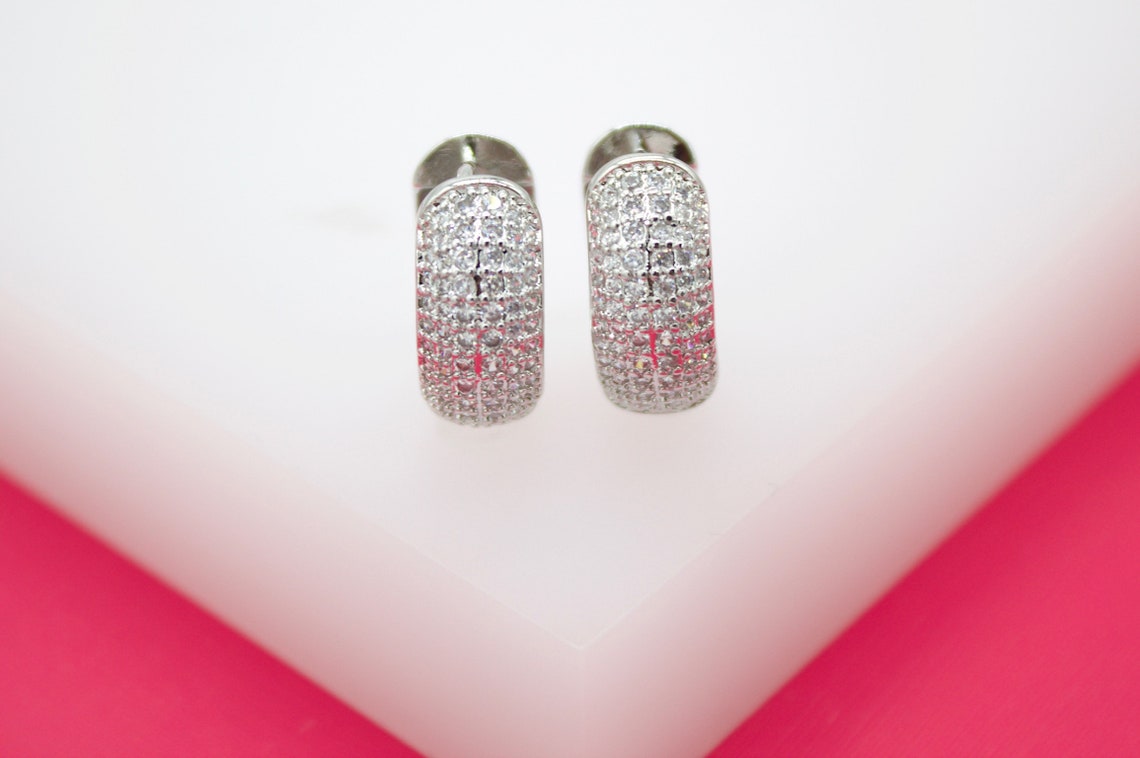 A pair of sterling silver huggie earrings encrusted with shimmering pavé cubic zirconia stones rests neatly on a white display block.