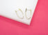 A pair of U-shaped gold hoop earrings encrusted with small pave diamonds rests on a white display block against a vibrant pink background.