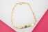 A polished gold-plated identification bracelet rests on a white and pink background.