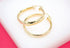 A pair of polished gold hoop earrings rests on a clean white surface against a bright pink background.