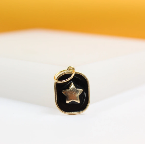 A gold pendant featuring a black enamel oval framing a raised gold star rests on a white surface against a warm yellow background.