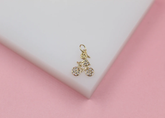 A gold bicycle charm with crystal accents rests on a white display block.