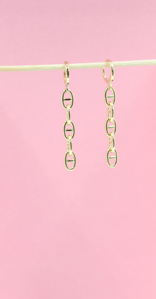 A pair of dangling gold chain-link earrings hangs gracefully against a soft pink background.