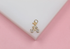 A gold bicycle pendant embellished with sparkling pave crystals rests on a white display surface against a pink background.