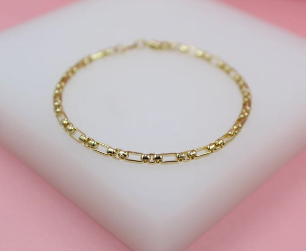 A delicate gold link bracelet rests on a white display pad against a soft pink background.