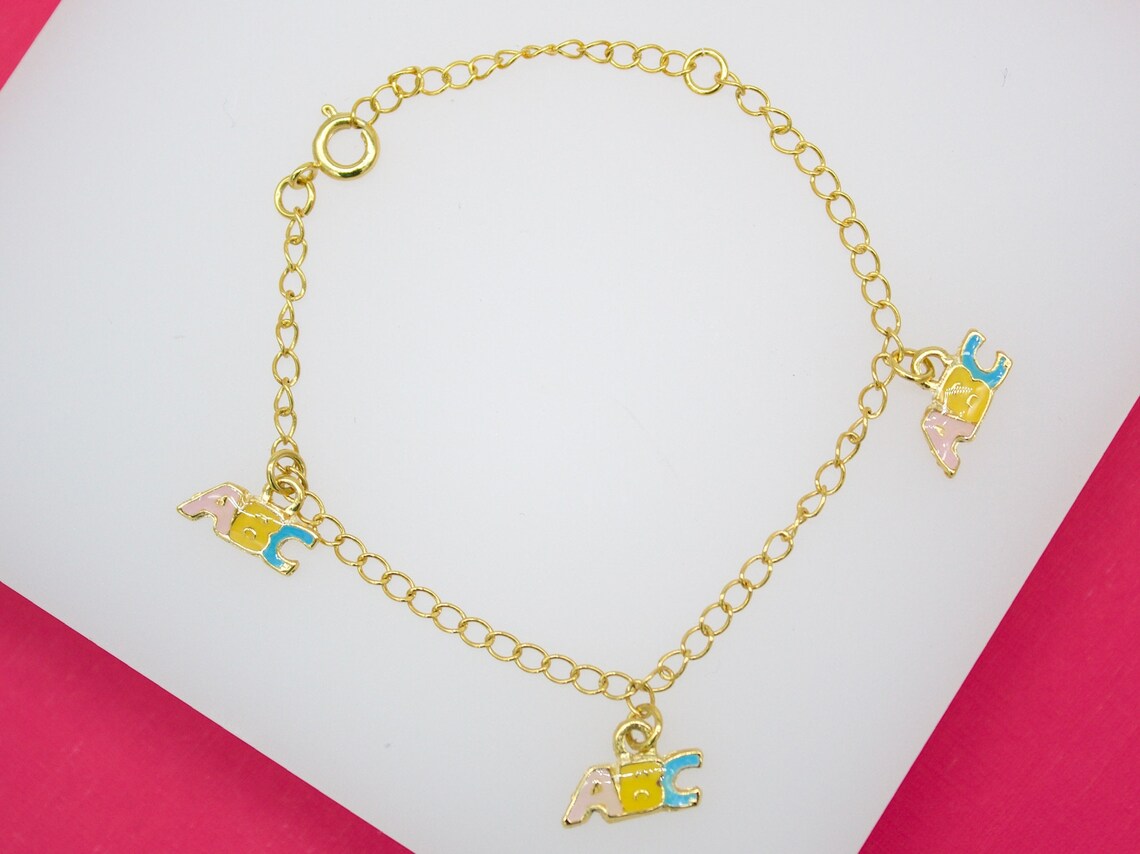 A delicate gold-plated chain bracelet features playful ABC alphabet letter charms enameled in pastel pink, yellow, and blue.