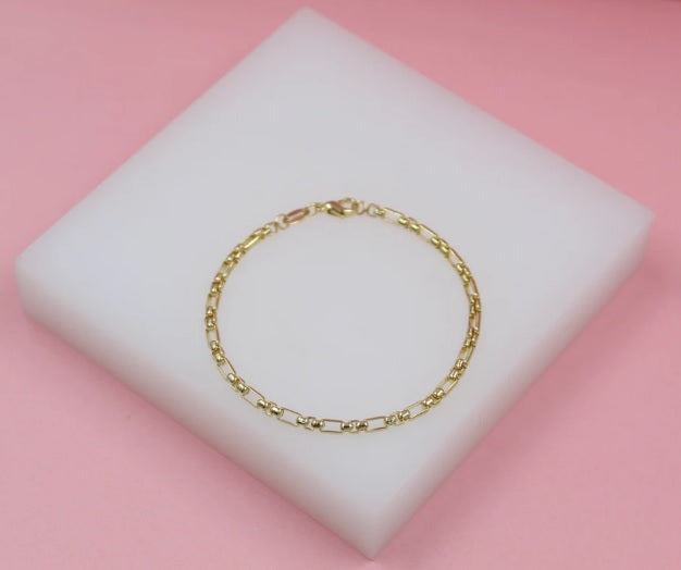 A delicate gold link bracelet rests gracefully on a white display pad against a pink background.