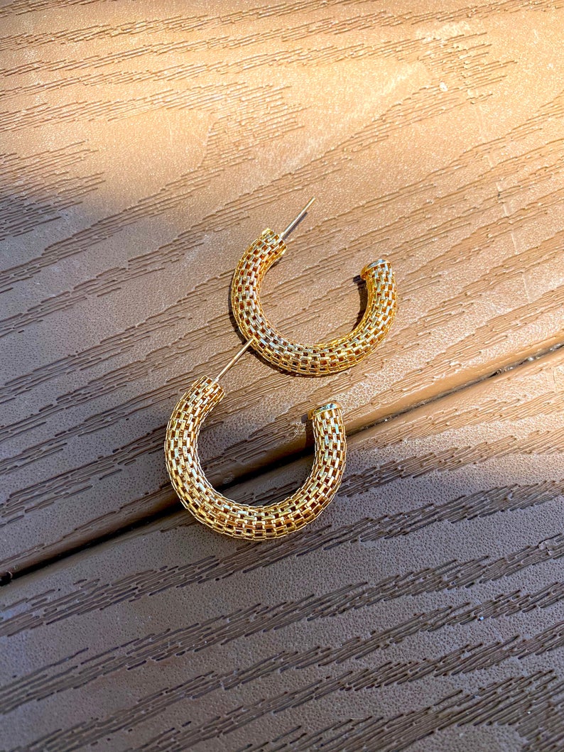 Two textured gold hoop earrings rest on a wooden surface.