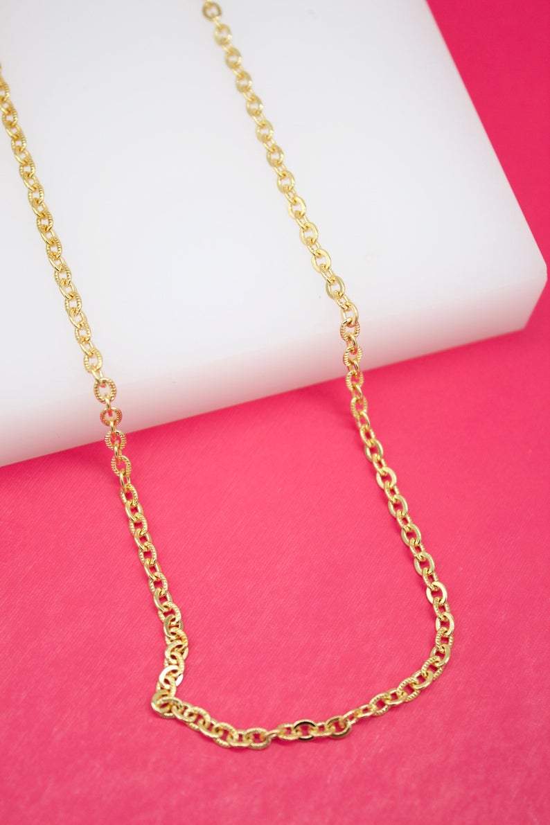 A delicate gold chain necklace drapes gracefully against a vibrant pink and white background.