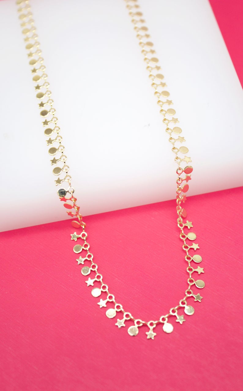 A delicate gold chain necklace drapes gracefully, featuring alternating star and circle charms against a vibrant pink and white background.
