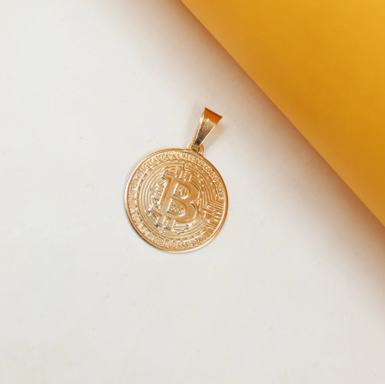 A shiny gold Bitcoin pendant rests against a white and yellow background.