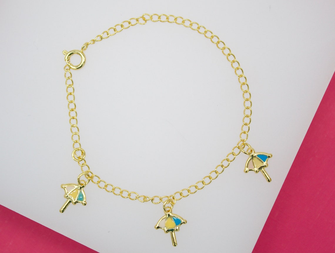 A delicate gold charm bracelet displays three colorful umbrella charms on a light background.