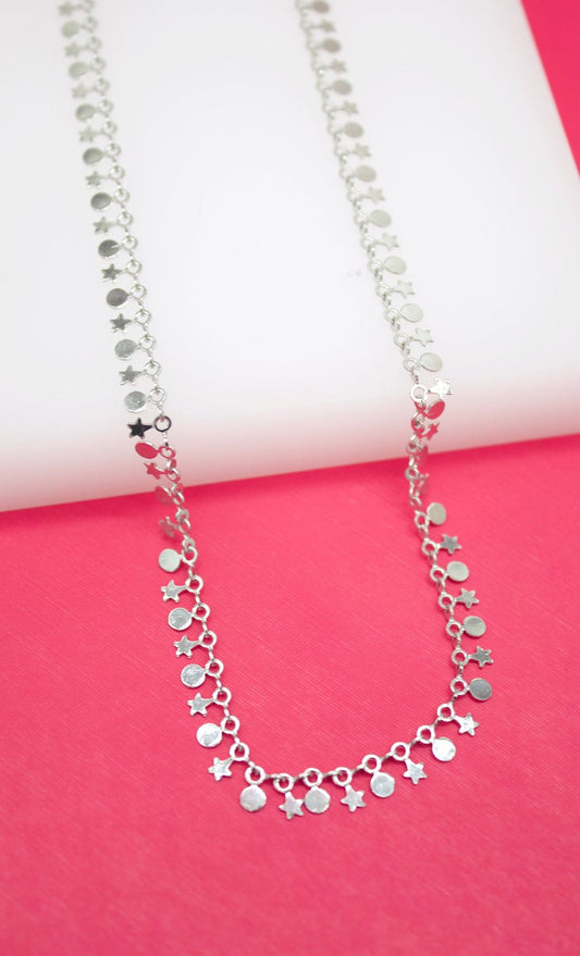 A silver charm necklace with alternating round and star-shaped pendants drapes against a vibrant pink and white background.