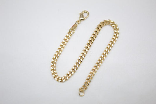 A gleaming gold cuban link chain bracelet rests on a neutral surface, showcasing its classic interlocking links and secure lobster clasp.