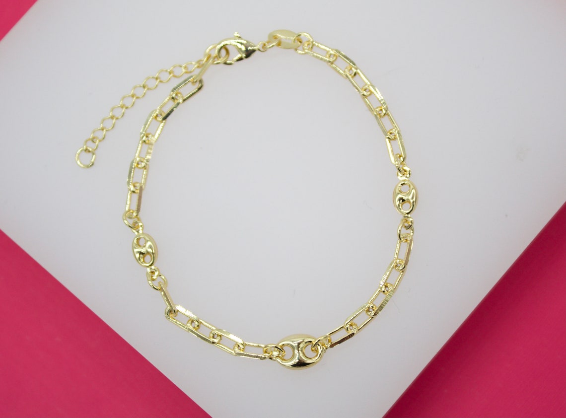 A gold-plated link bracelet featuring alternating oblong and rounded geometric elements rests on a white display surface.