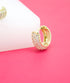 A sparkling gold huggie hoop earring encrusted with small pave crystals rests on a white block against a vibrant pink background.