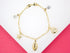 A gold charm bracelet features whimsical ocean-themed charms, including a seashell, starfish, fish, and sparkling crystal stars.