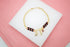 A gold chain bracelet adorned with black and red beads features dangling charms including an elephant, a figa, and an evil eye.