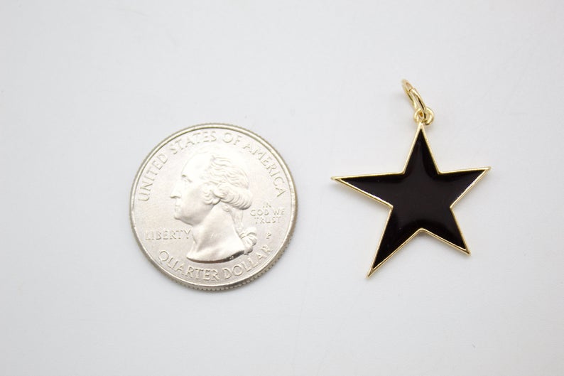 A gold-rimmed black enamel star charm rests next to a US quarter coin for scale on a white surface.