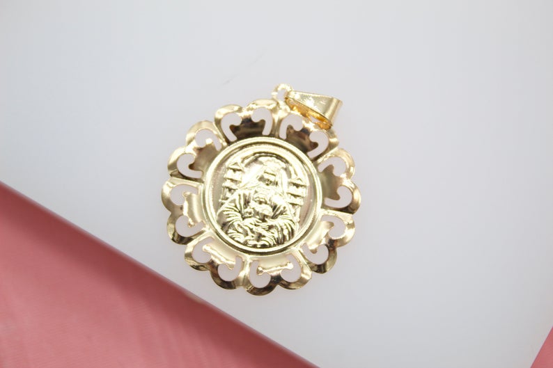 A round gold pendant featuring an engraved image of the Virgin Mary rests on a light-colored surface.