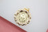 A round gold pendant featuring an engraved image of the Virgin Mary rests on a light-colored surface.