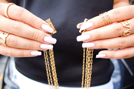 A woman with light pink manicured nails showcases gold chain jewelry and rings.