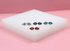 A collection of gold evil eye stud earrings in red, light blue, dark blue, and turquoise rest on a white block against a pink background.