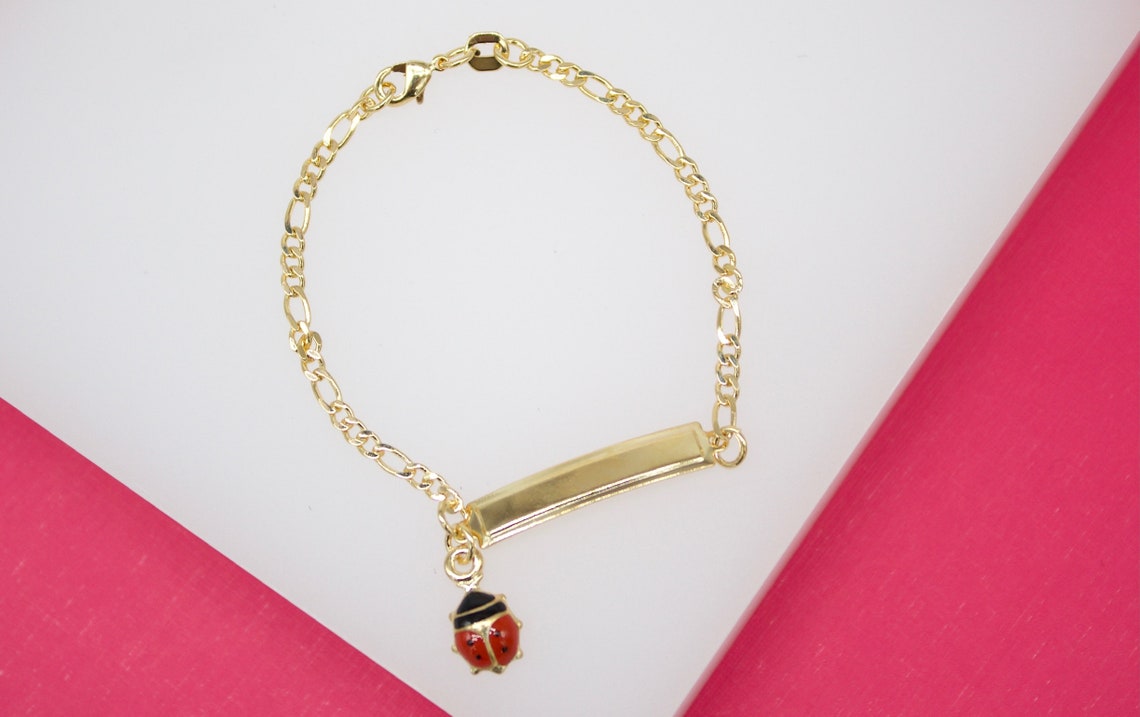 A gold-plated ID bracelet features a delicate chain and a dangling red and black ladybug charm.