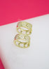 Two gold huggie hoop earrings featuring pavé diamond heart motifs rest on a white surface against a pink background.