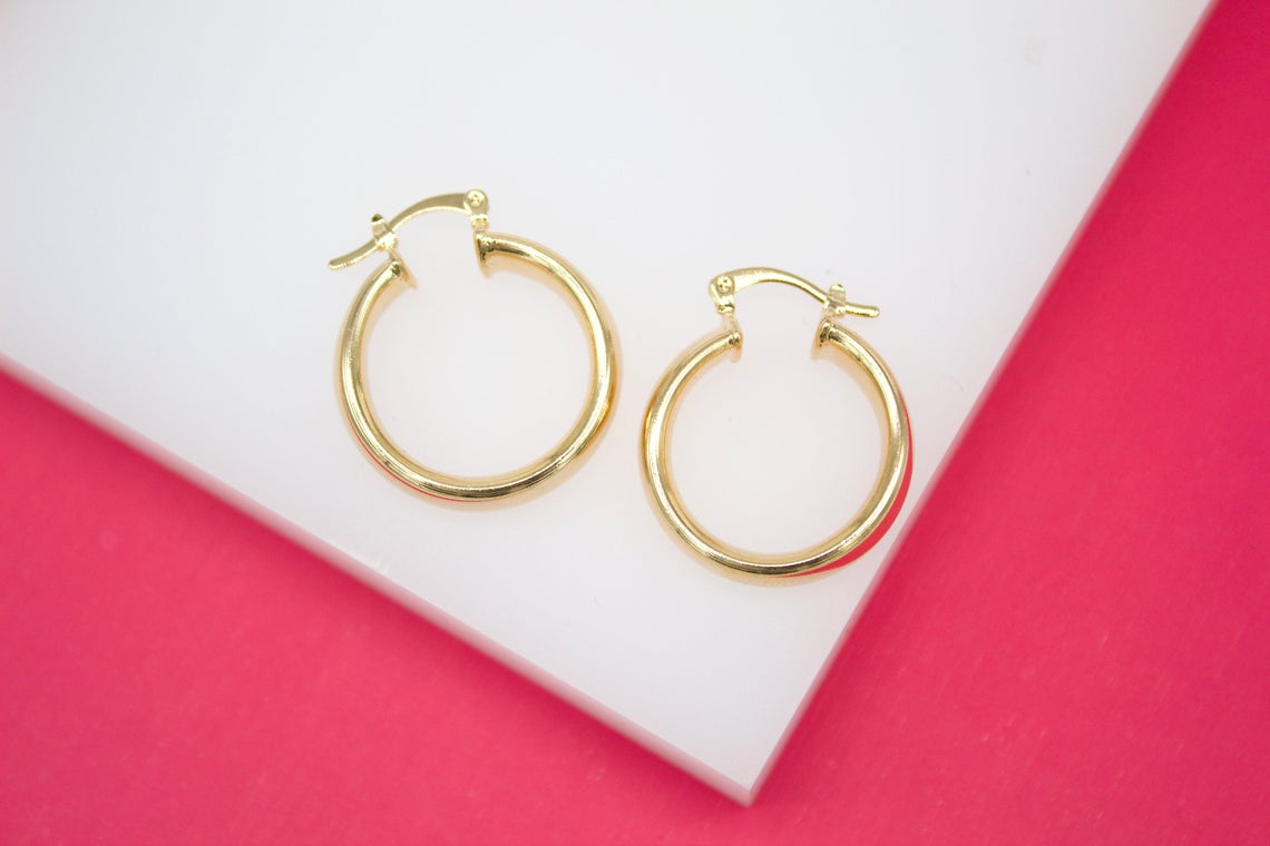 A pair of polished gold hoop earrings rests neatly on a white display against a vibrant pink background.