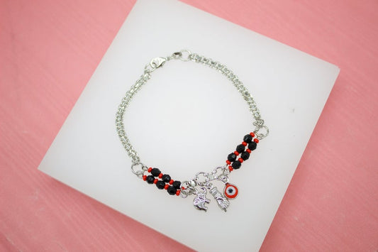 A silver charm bracelet with black and red beads rests on a white display against a pink background.