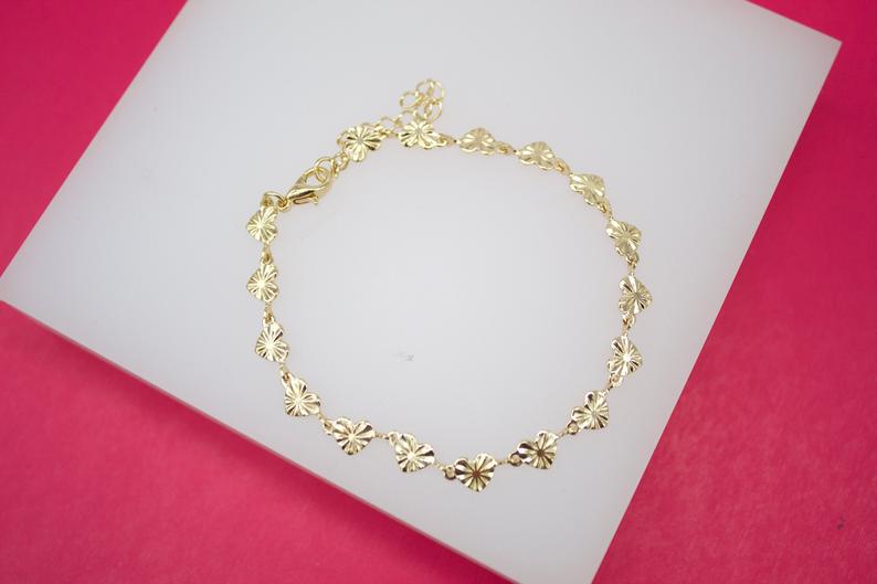 A delicate gold-plated heart-shaped link bracelet rests on a white display surface against a vibrant pink background.