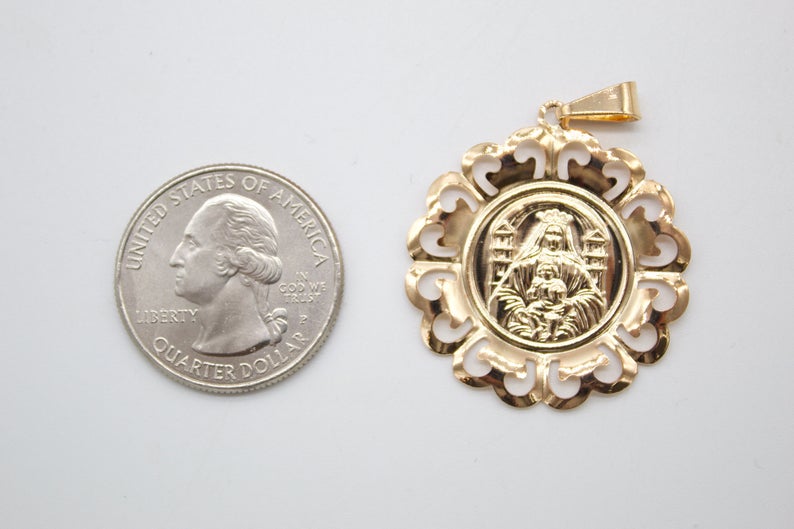 A round gold pendant featuring a religious figure sits next to a US quarter coin for scale.