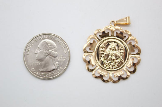 A round gold pendant featuring a religious figure sits next to a US quarter coin for scale.