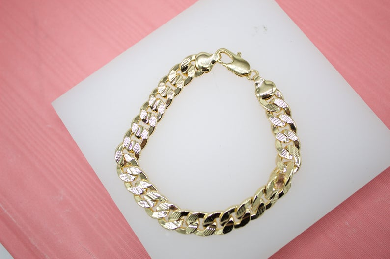 A gold curb chain bracelet rests on a white display pad against a pink background.