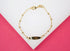 A delicate gold ID bracelet with interspersed beads lies against a pink and white background.