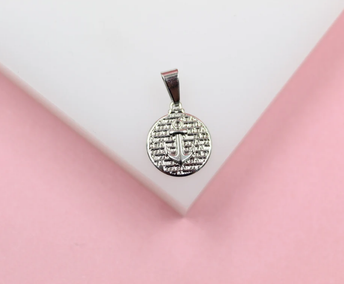 A silver anchor pendant featuring a textured background lies on a white and pink surface.