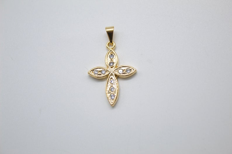 A delicate gold cross pendant rests against a plain background, sparkling with embedded cubic zirconia stones in each of its four petal-like arms.