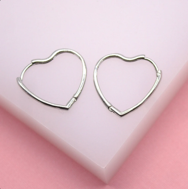 A pair of silver heart-shaped hoop earrings rests on a pale pink display stand.