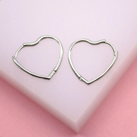 Two silver heart-shaped hoop earrings rest on a light pink display block.