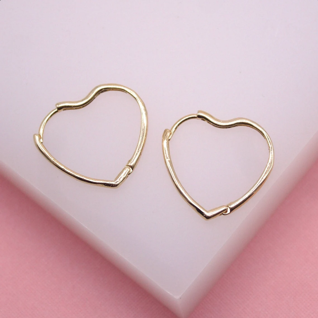 A pair of shiny gold heart-shaped hoop earrings rests on a soft pink surface.