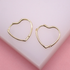 A pair of delicate gold heart-shaped hoop earrings rests on a soft pink background.